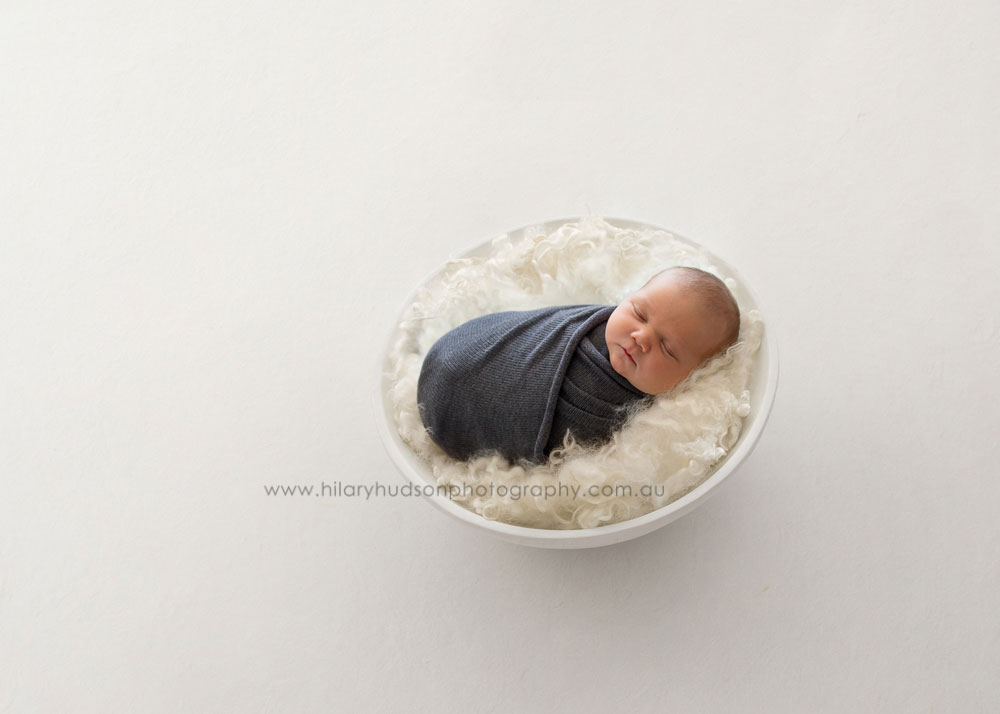 A white bowl with a little baby boy wrapped up and sleeping peacefully