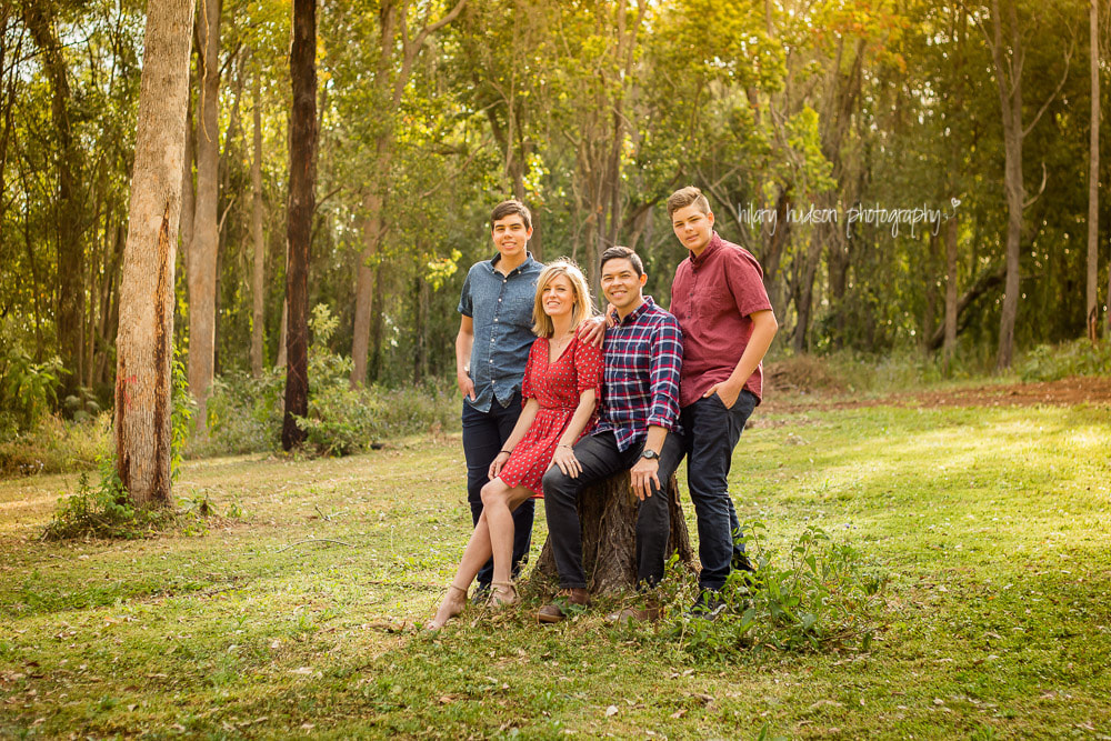 A family of four, with two grown up boys, sitting on a tree stump in a rural field