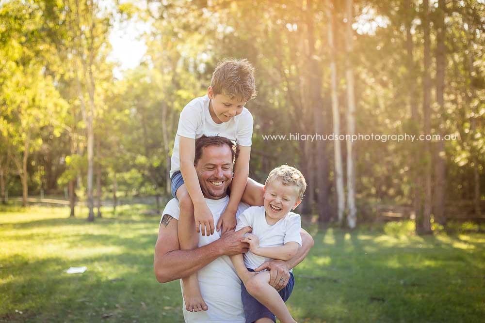A dad having lots of fun laughing with his two boys - one on his shoulder and one on his hip.