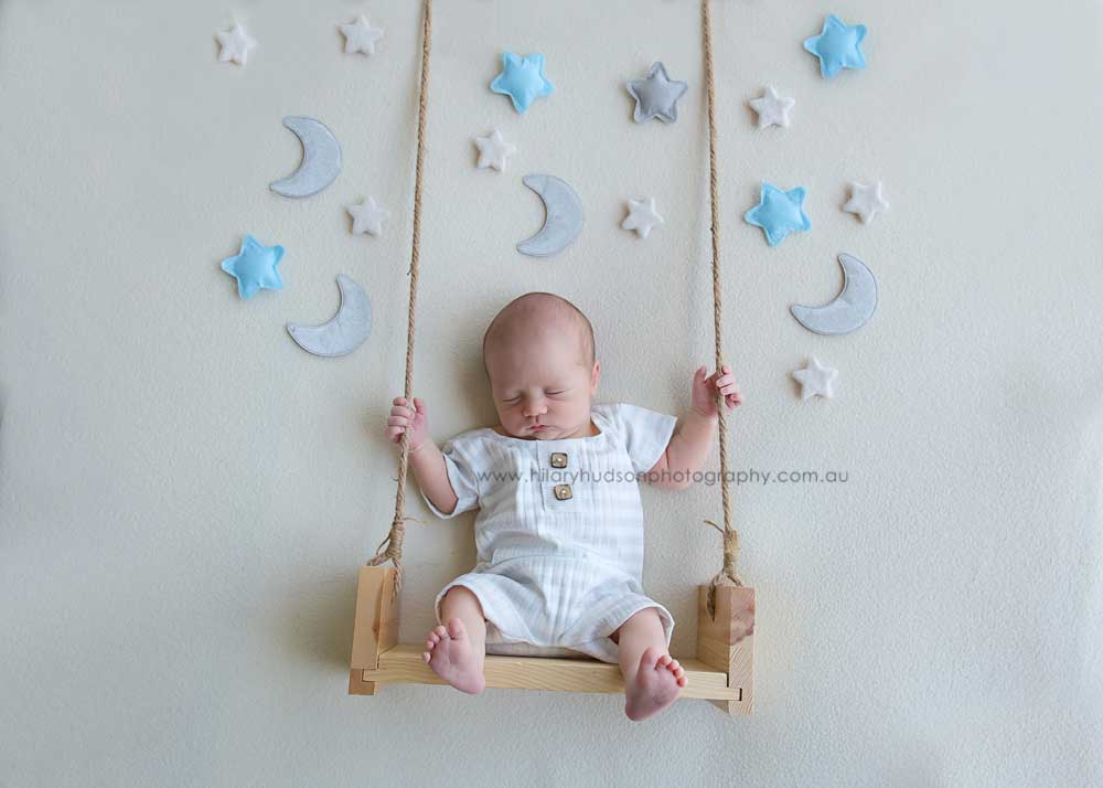 Sleeping baby sitting on a swing, cream background surrounded by stars and moons