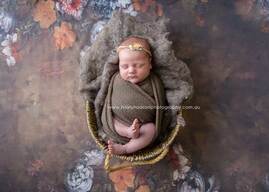 newborn baby curled up in a wicker basket, on a nature backdrop of browns and autumn tones
